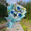 Ein Str wiederhandgefertigter blau-weißer Blumenstrauß aus Häkelarbeit, eingewickelt in hellblauen Papier und Papiertupfer.