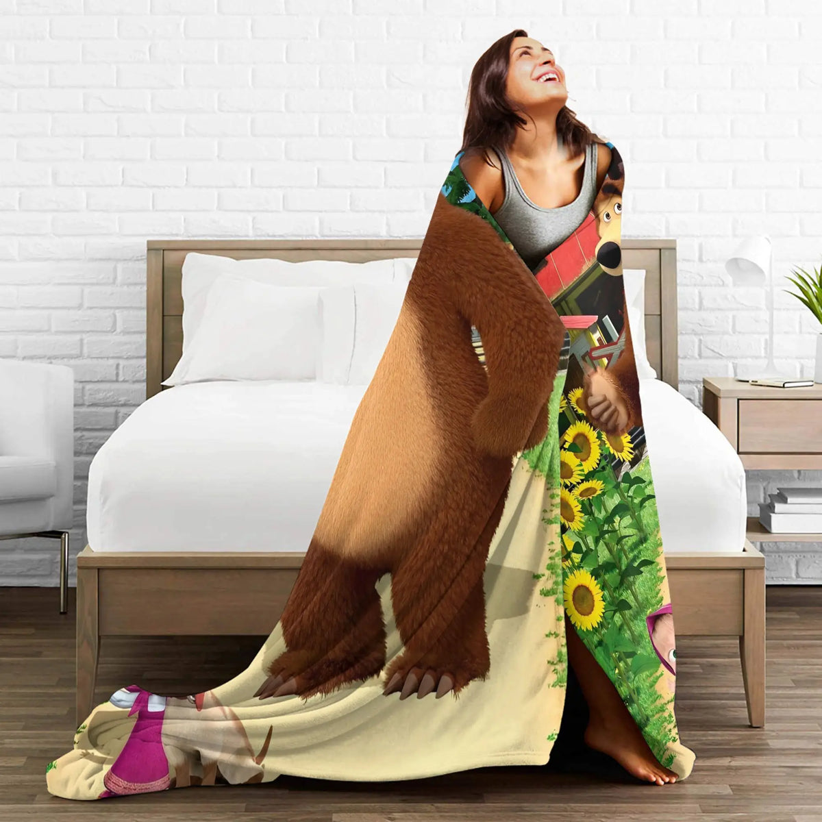 A woman is lying on a bed with a flannel throw blanket featuring a Masha and Bear cartoon design.