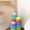 A set of colorful, disposable toilet brush heads stacked in a holder next to a wall-mounted dispenser.