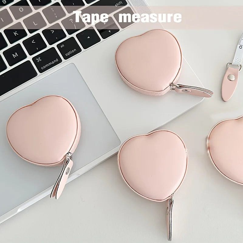 A pink PU leather tape measure with a heart-shaped clip is shown next to a laptop keyboard.