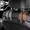 Car headrest hooks in brown leather attach to a black car seat for bags and organizers