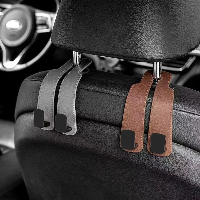 Car headrest hooks in brown leather attach to a black car seat for bags and organizers