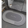 A gray bath mat with a non-slip rubber base is placed on a tiled floor in a bathroom setting.
