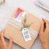 Hands are tying a natural twine bow on a kraft paper gift box with a thank you tag.