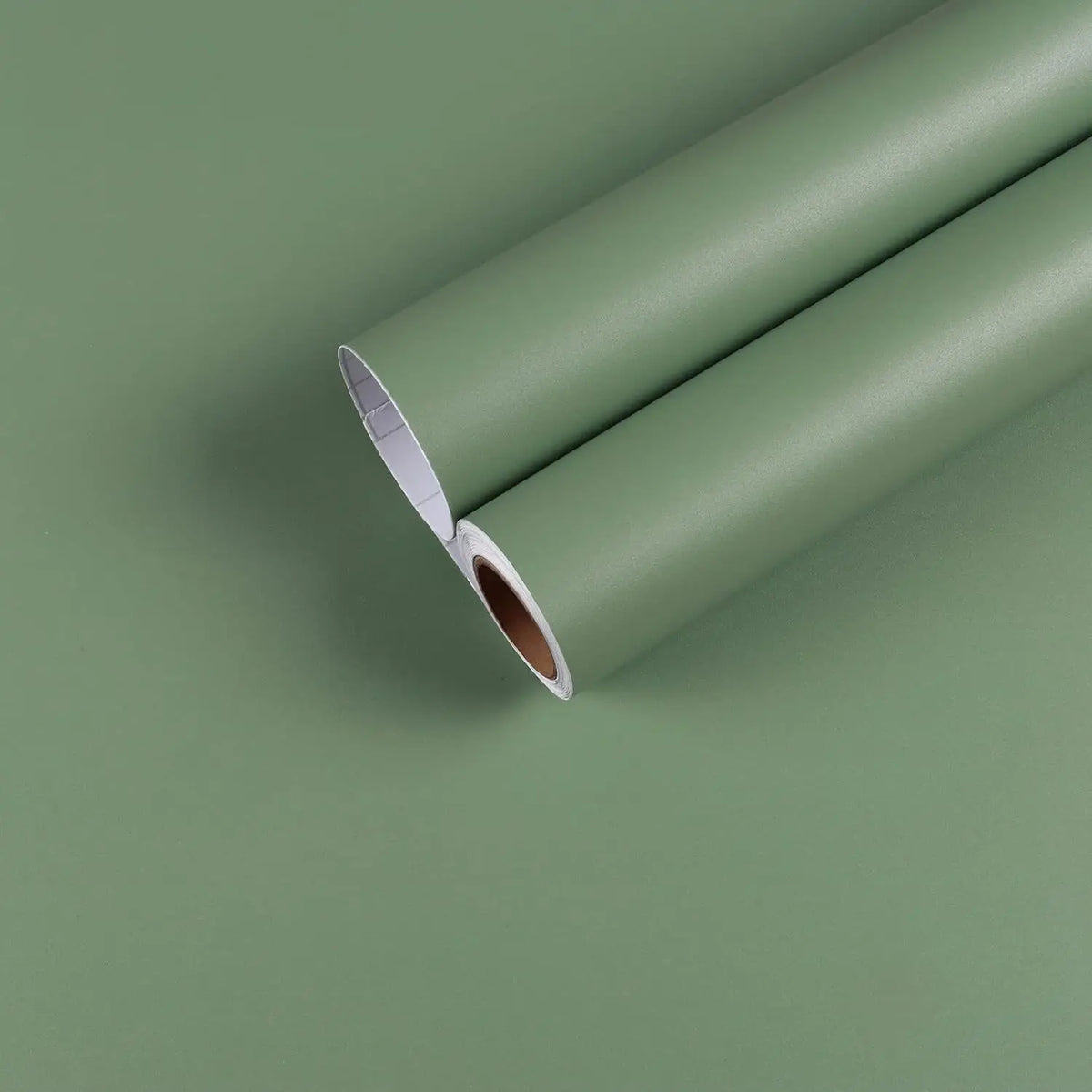 Roll of self-adhesive matte white vinyl wallpaper lying on a green surface.