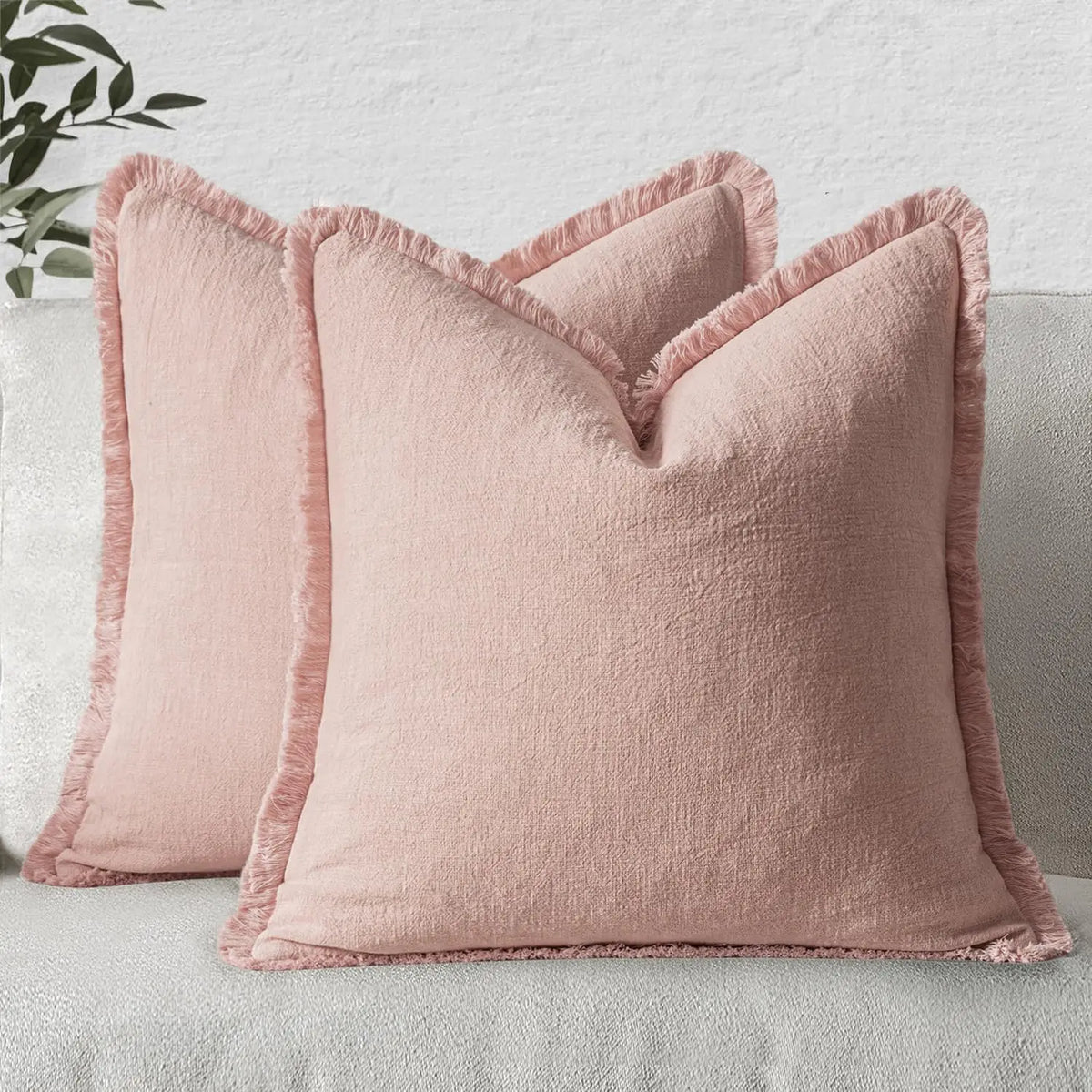 A light pink boho fringe throw pillow cover with a natural linen texture resting on a light gray sofa.