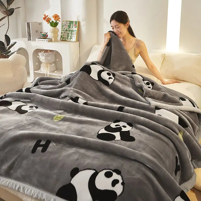 Graue Plüschdecke mit wiederholtem schwarz-weißem Panda-Muster auf einem weißen Sofa.