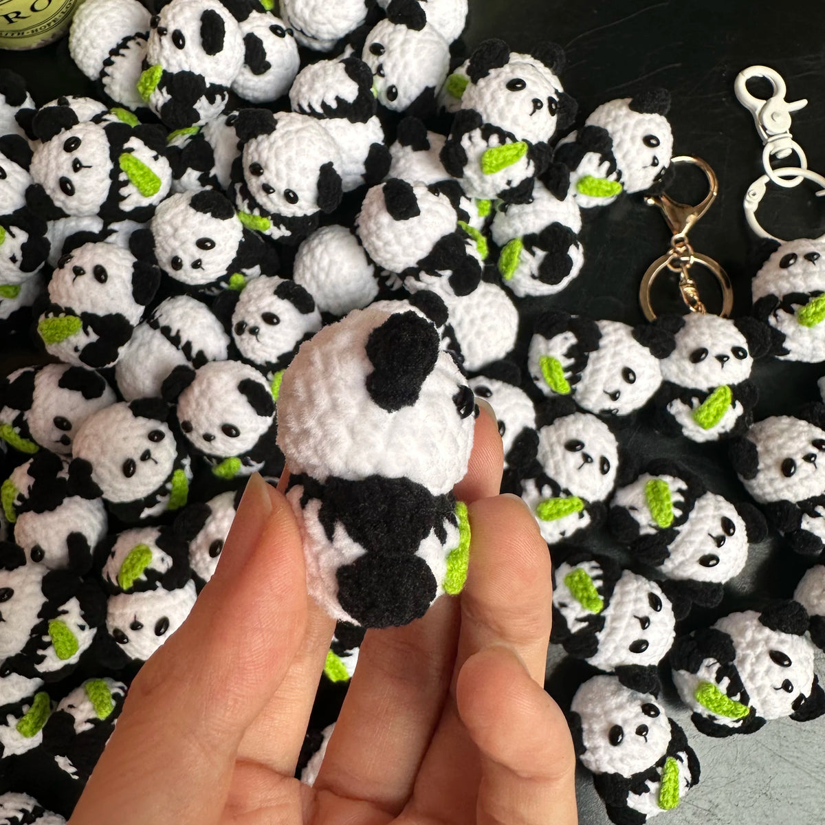 A hand holds a handmade crochet kitten keychain featuring a cute panda and cartoon animal charm.