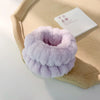 A stack of light purple microfiber wrist sweatbands and scrunchies for face washing placed on a beige tray.