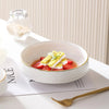 A white ceramic soup bowl filled with strawberries, herbs, and a light dressing, set on a white plate.