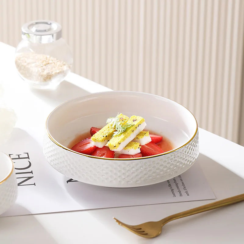 A white ceramic soup bowl filled with strawberries, herbs, and a light dressing, set on a white plate.