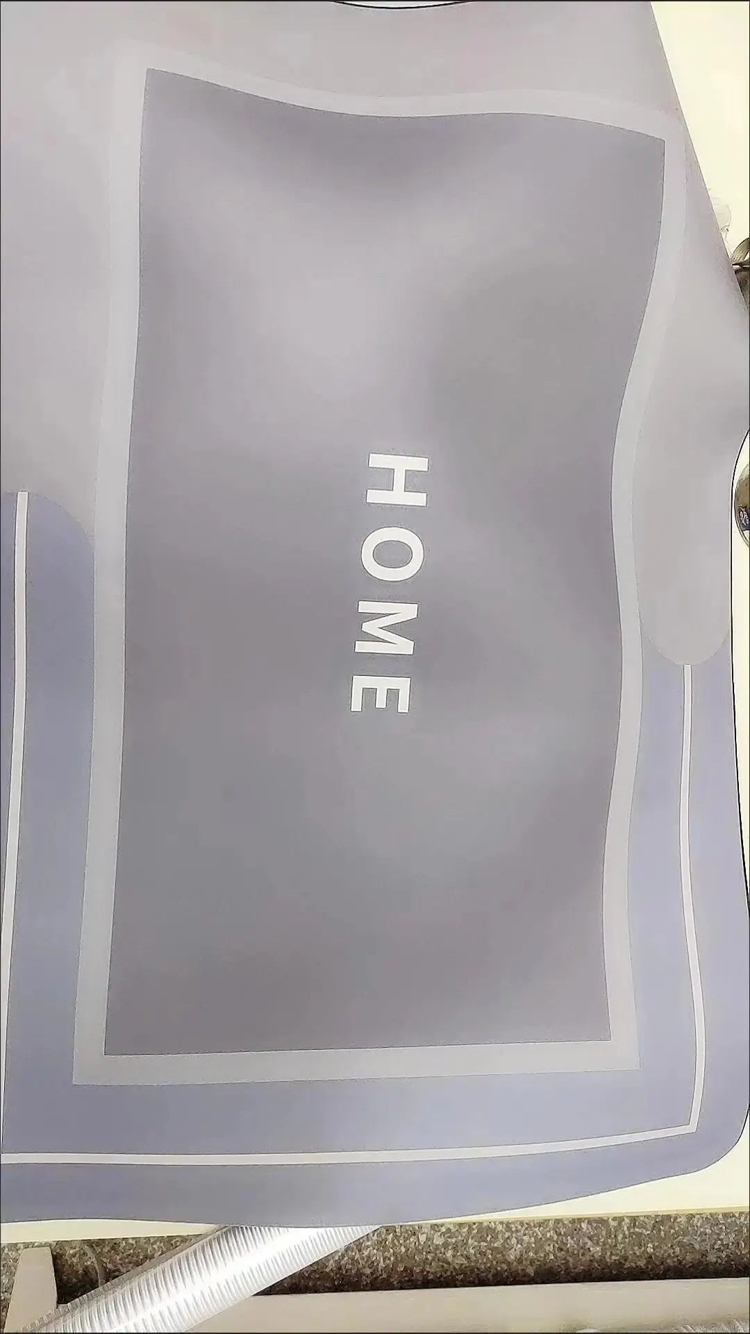 A gray bath mat with the word HOME printed on it, featuring a non-slip rubber base.