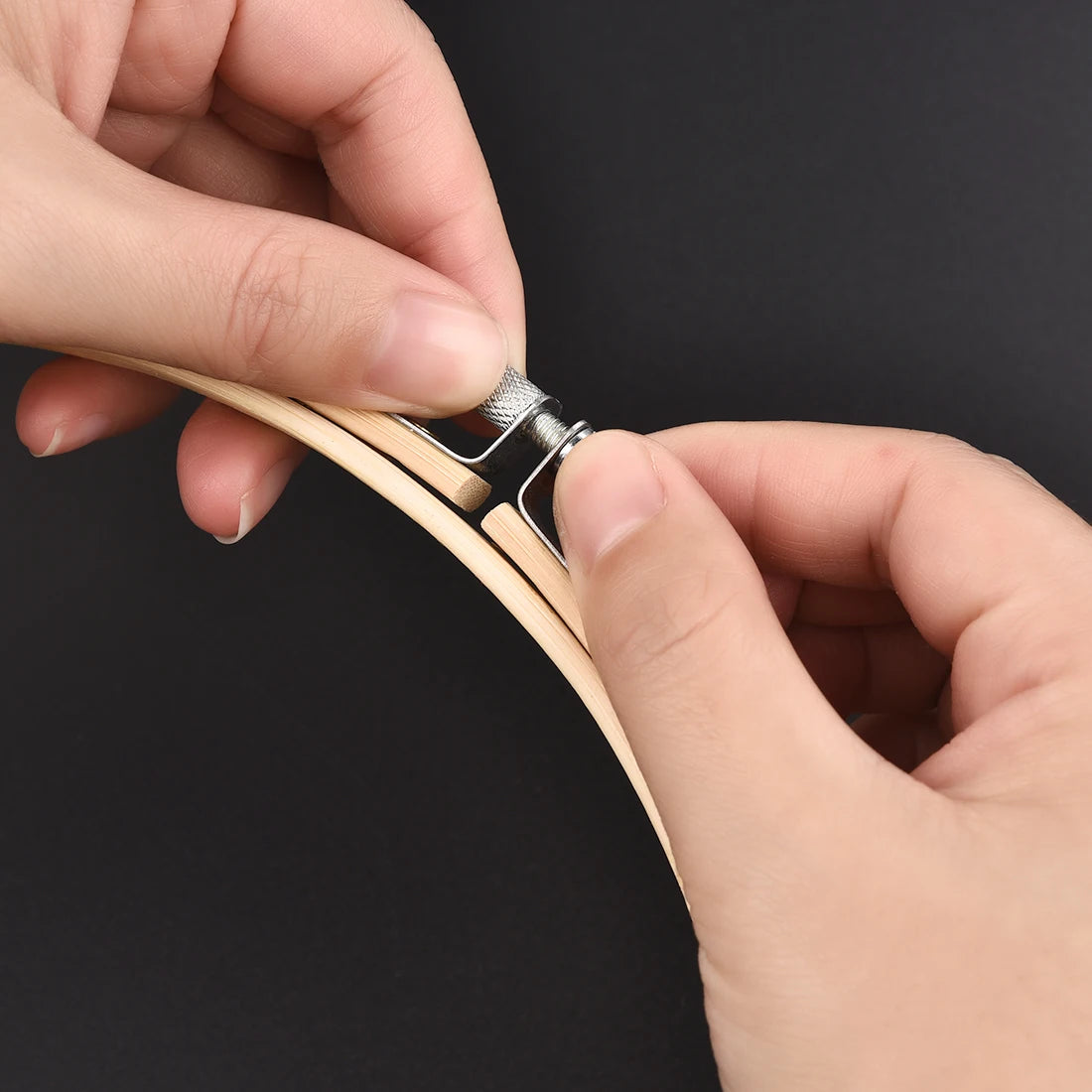 Hands are adjusting a bamboo embroidery hoop with an adjustable screw mechanism.