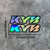 A pair of motorcycle fork stickers featuring the letters KYB in a gradient of blue, green, and orange on a gray textured back