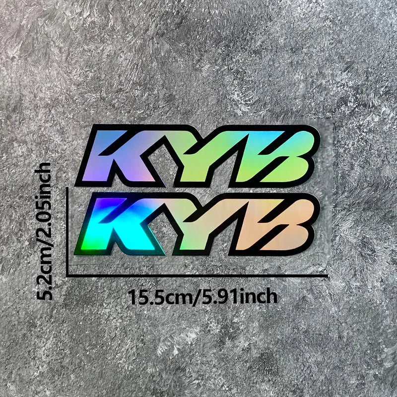 A pair of motorcycle fork stickers featuring the letters KYB in a gradient of blue, green, and orange on a gray textured back