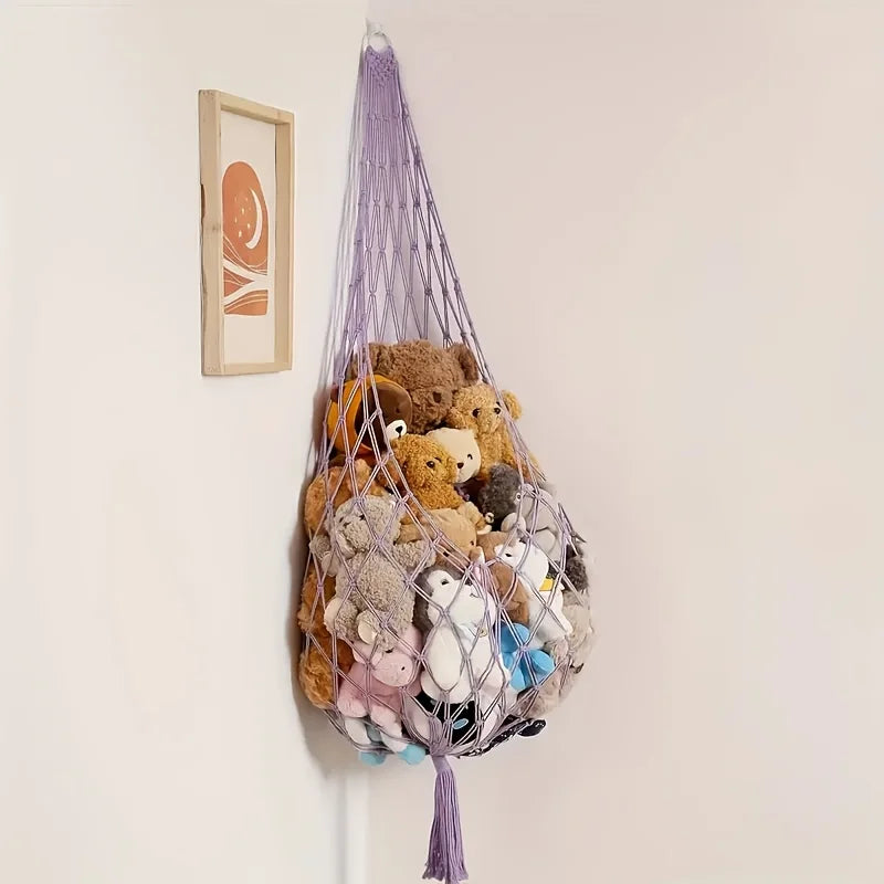 A macrame hammock filled with various stuffed animals hanging on a white wall.