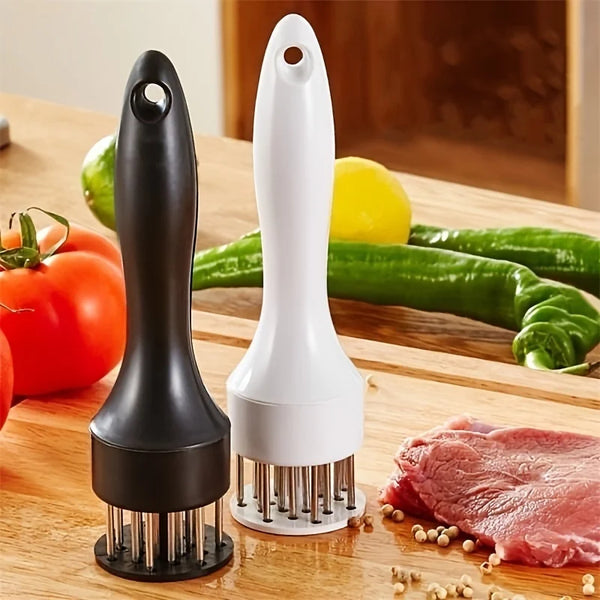 A black and white meat tenderizer tool with multiple metal needles resting on a wooden cutting board next to fresh vegetables