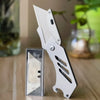 A white stainless steel folding utility knife with a visible blade is displayed next to its protective sheath.