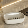 A white double-layer draining soap dish with a non-slip base resting on a marble surface.