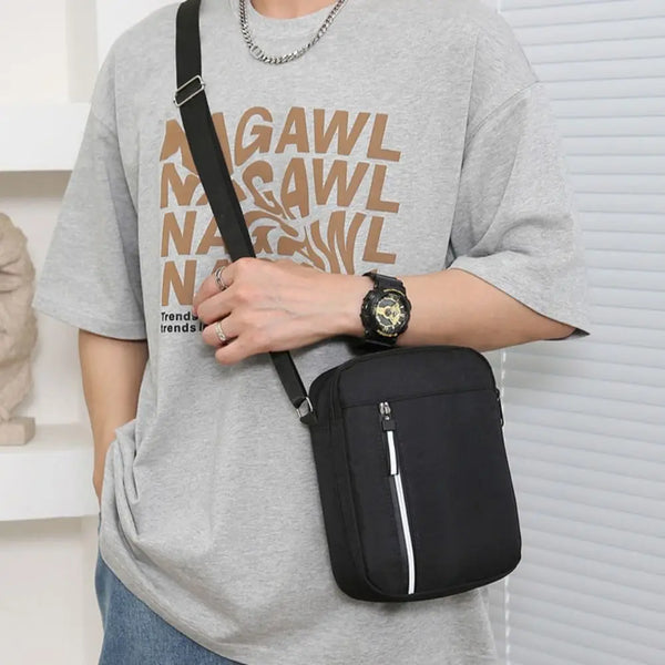 A man wearing a gray t-shirt holds a black nylon crossbody bag with a gold watch.