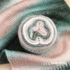 A roll of soft, colorful gradient yarn in pink and grey tones displayed on a green knitted fabric.