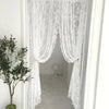 Rideau transparent à broderie florale blanche suspendu dans un cadre de porte blanc.
