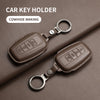 Brown genuine leather car key holder with a metal ring, shown on a dark brown surface.