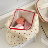 A quilted, cream-colored makeup bag with a red zipper and heart pattern is shown open on a white surface.