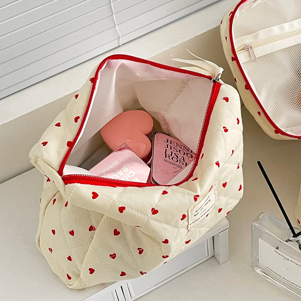 A quilted, cream-colored makeup bag with a red zipper and heart pattern is shown open on a white surface.