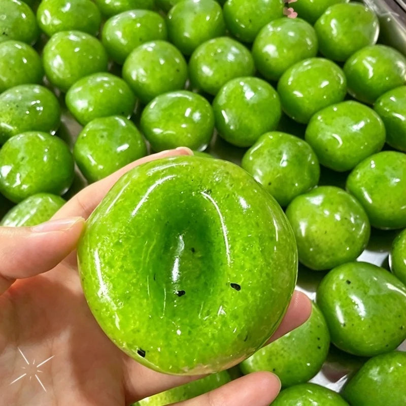 A hand holds a bright green handmade squishy stress relief fidget ball surrounded by many similar balls.