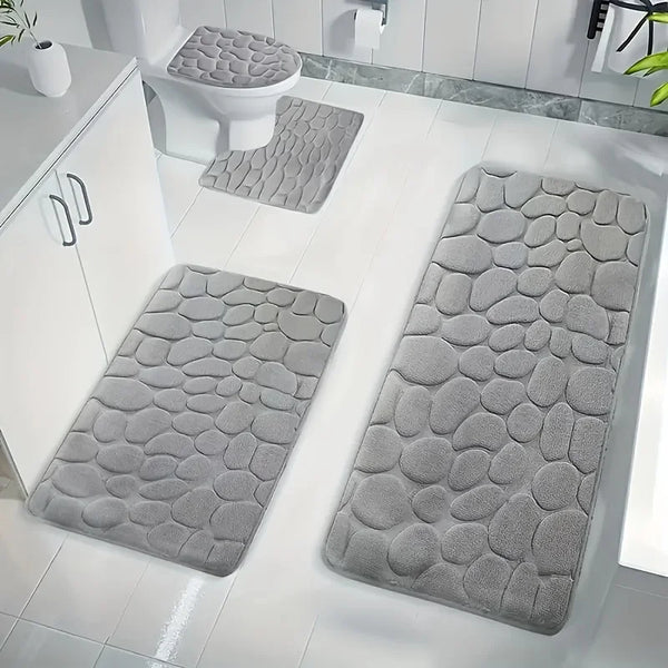 Gray pebble-embossed quick-dry bath mat placed on a white bathroom floor next to a toilet.