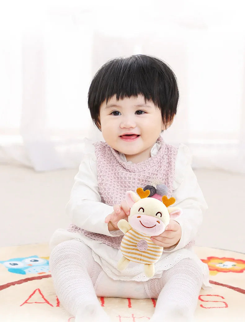 A smiling baby holds a soft plush toy of a cartoon animal with ears and a nose.