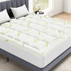 Un surmatelas de matelas en bambou viscose à quilting blanc posé sur un cadre de lit gris avec un motif de feuilles vert clai