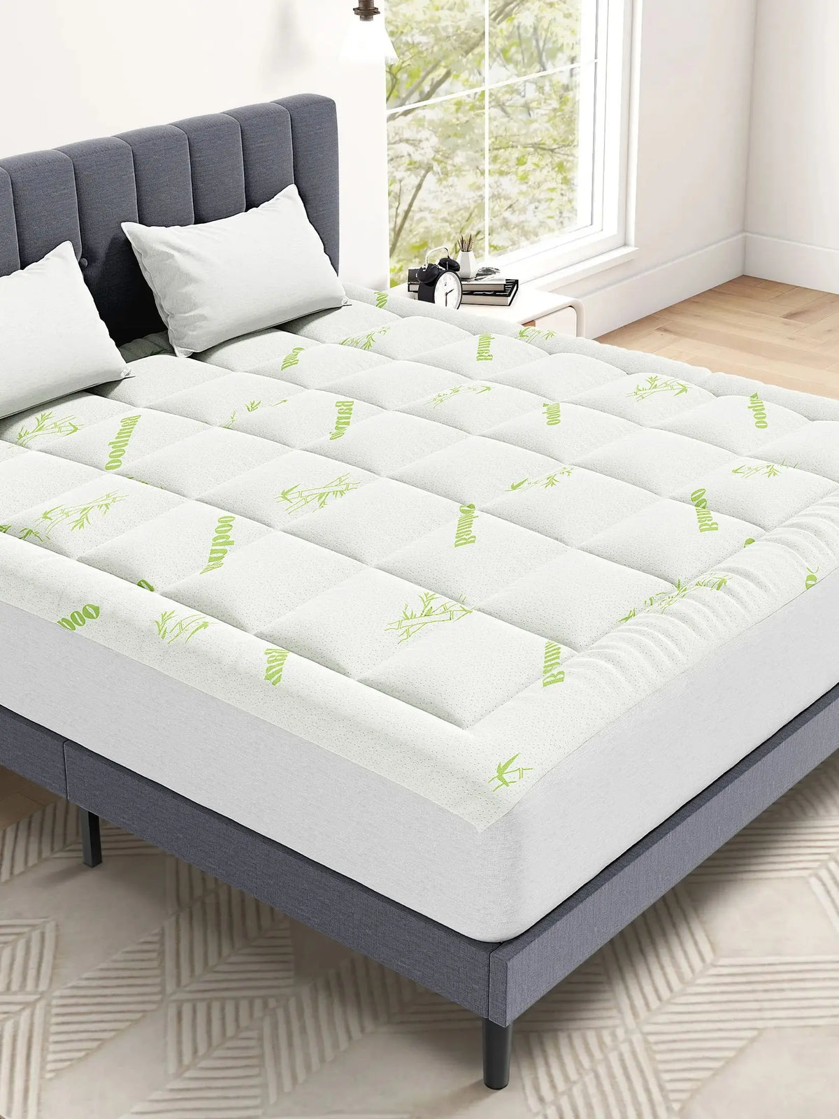 Un surmatelas de matelas en bambou viscose à quilting blanc posé sur un cadre de lit gris avec un motif de feuilles vert clai