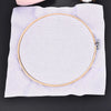 A round white bamboo embroidery hoop with a gold rim and an adjustable screw is placed on a white cloth.