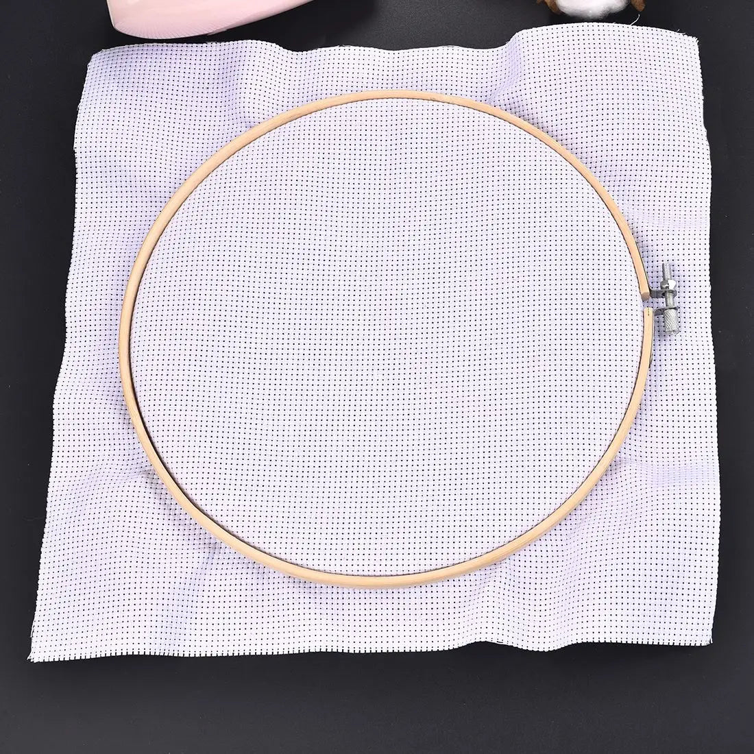 A round white bamboo embroidery hoop with a gold rim and an adjustable screw is placed on a white cloth.