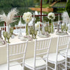 A long table set for a wedding or formal dinner featuring white chairs, green glassware, and floral arrangements.