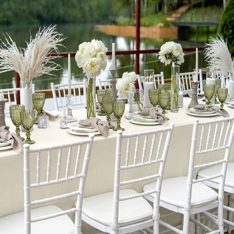 A long table set for a wedding or formal dinner featuring white chairs, green glassware, and floral arrangements.