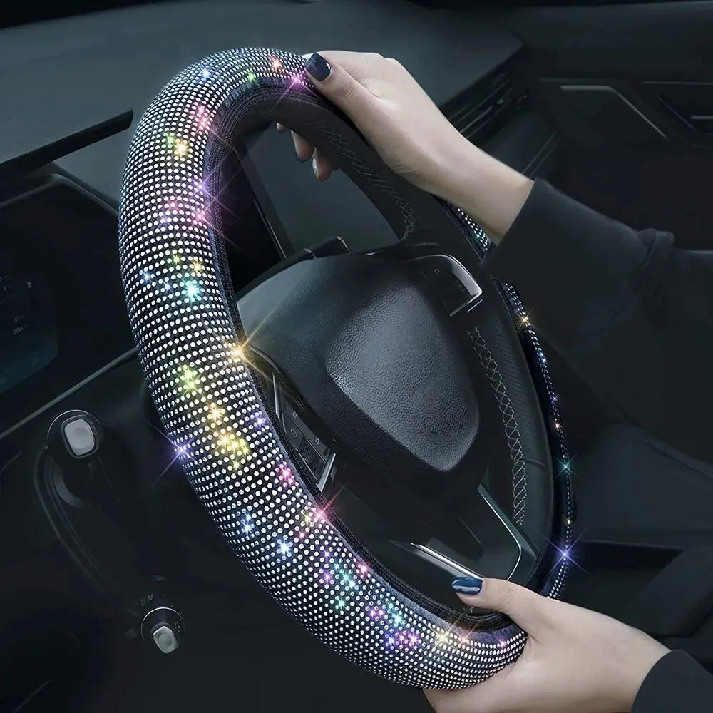 A hand is gripping a crystal rhinestone steering wheel cover on a car's steering wheel.