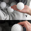 A hand is holding a white reusable laundry ball, demonstrating the product for fluffier and faster drying.
