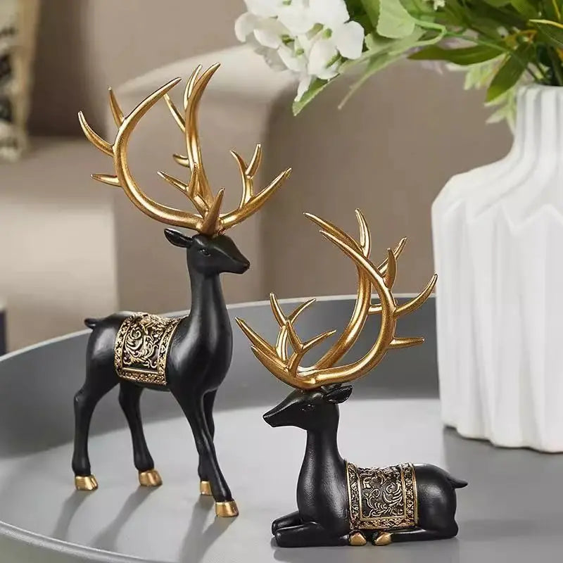 A set of two resin deer figurines, one standing and one lying down, in black and gold finish.