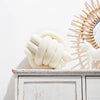 A cream-colored, hand-knotted velvet throw pillow shaped like a stylized white horse sits on a white wooden shelf.