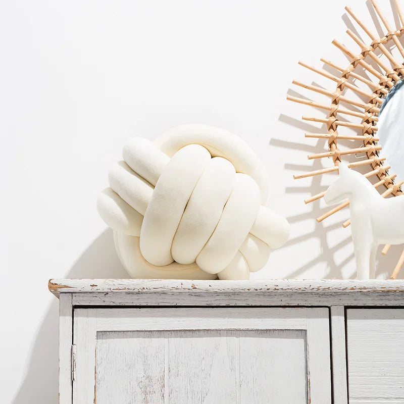 A cream-colored, hand-knotted velvet throw pillow shaped like a stylized white horse sits on a white wooden shelf.
