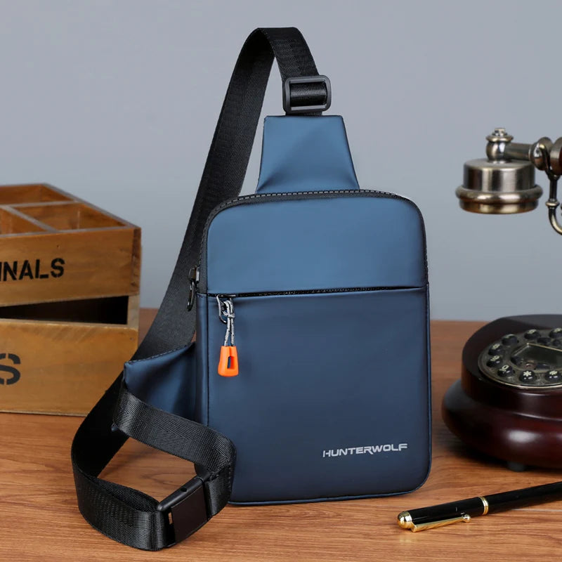 A dark blue compact men's crossbody chest bag with black strap resting on a wooden surface.