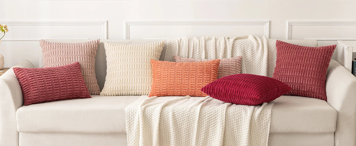 A set of four textured throw pillows in shades of pink, peach, and terracotta resting on a light-colored sofa.