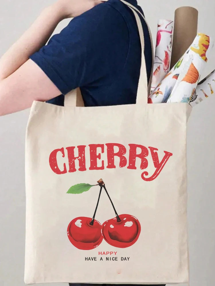 A beige canvas tote bag featuring a red cherry graphic and the text Happy Have a Nice Day.