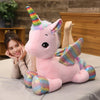 A pink unicorn plush toy with a rainbow horn and colorful accents is being held by a woman.