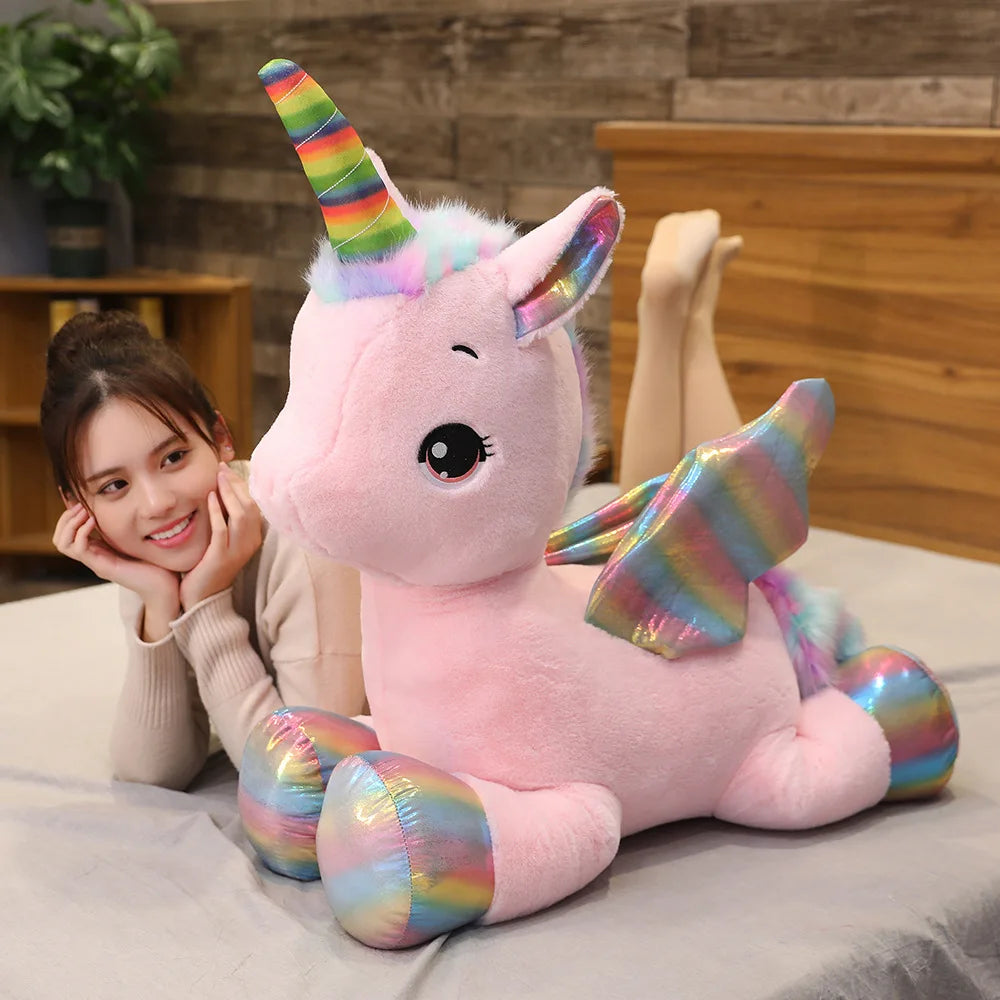 A pink unicorn plush toy with a rainbow horn and colorful accents is being held by a woman.