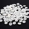 A pile of 100 white acrylic pearl spacer beads for jewelry making scattered on a black surface.