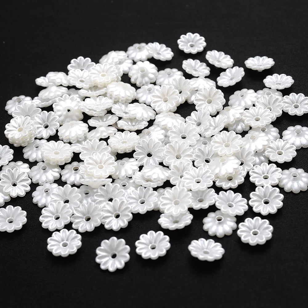 A pile of 100 white acrylic pearl spacer beads for jewelry making scattered on a black surface.